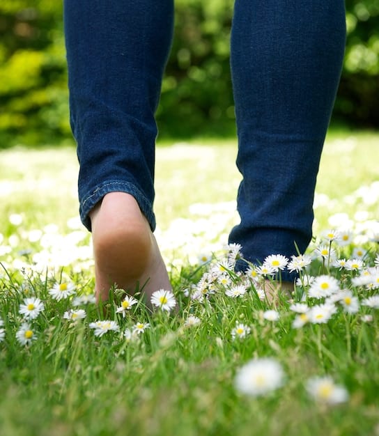 A close-up of feet walking on grass, symbolizing grounding, connection with earth, and focus on the present moment.