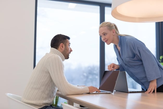 Two colleagues in an open-plan office are facing each other, engaged in a focused conversation. One is actively listening with a slight smile, while the other gestures while speaking. The environment is bright and modern but calm.