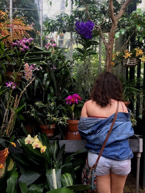 A person tending to a small balcony garden filled with various plants and flowers in pots. The scene highlights the possibility of creating a natural oasis in an urban environment.