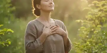 Person practicing mindful breathing in a serene natural setting, hands on chest, eyes closed in calm focus.